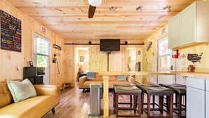 Een cabin met houten vloer, een bank, een eettafel met stoelen, een aan de muur bevestigde televisie en een vluchtweg aanduiding.