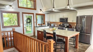A kitchen with a central island, white cabinets, stainless steel appliances, and a wooden staircase. - Luxury Lakefront Retreat, Hot Tub, Game Room, Views (Nisswa)