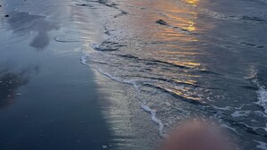 Ein Strand mit Sonnenuntergang, Wellen und einem Steg mit Menschen.
