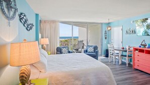 Ein Schlafzimmer mit einem großen Bett, einem Schreibtisch und einem Stuhl, Meerblick und einem Balkon mit Tisch und Stühlen.