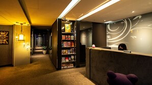 A reception area with a reception desk, a bookshelf with books, a plush toy, and a sign indicating no smoking. - Hotelshere Taipei (Taipei)