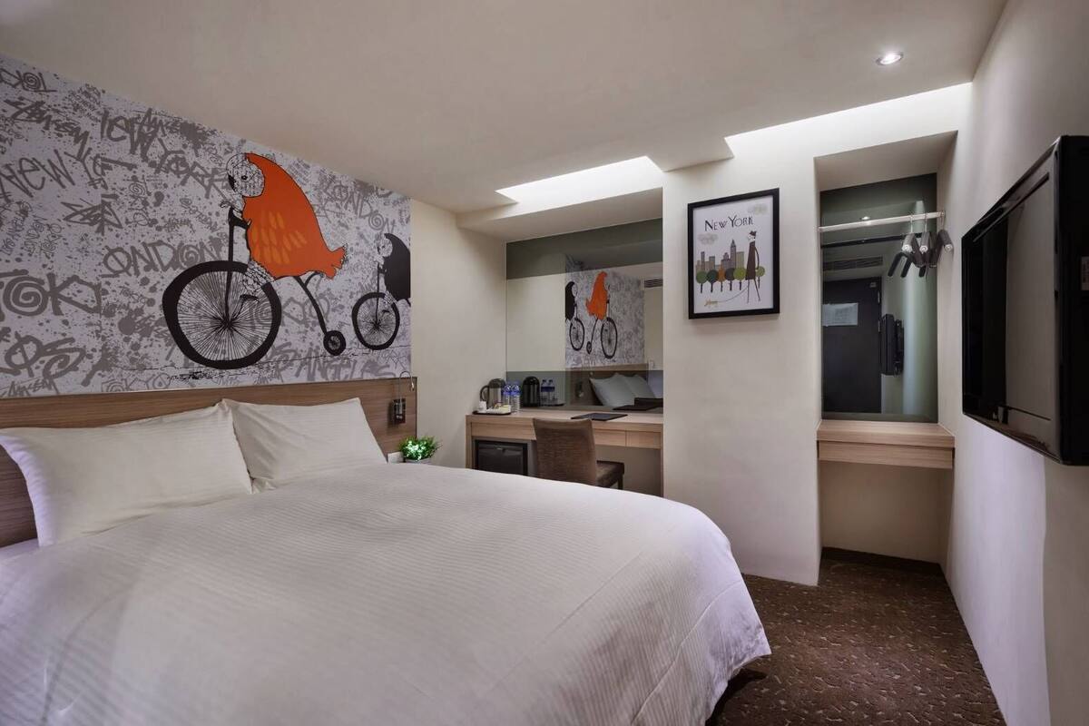 A hotel room with a large bed, a desk, a mirror, and a wall with graffiti art.