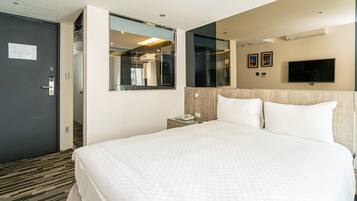 A hotel room with a large bed, a bedside table with a phone, a mirror, and a TV mounted on the wall.
