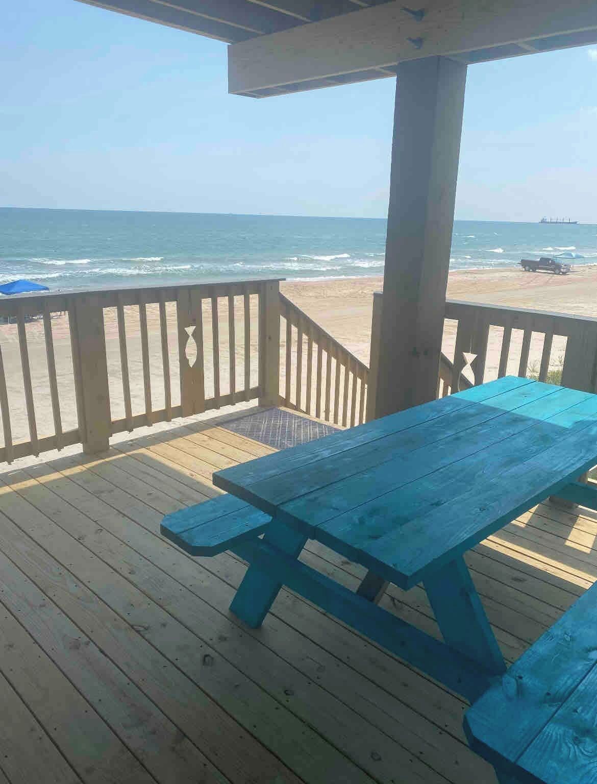 A wooden deck with a picnic table and a railing overlooking a beach.