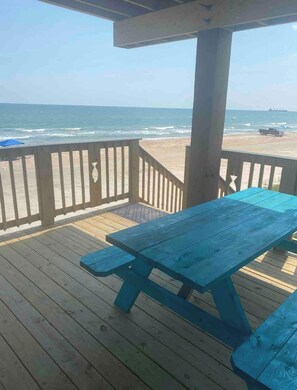 Une terrasse en bois avec une table de pique-nique et une rambarde donnant sur une plage.