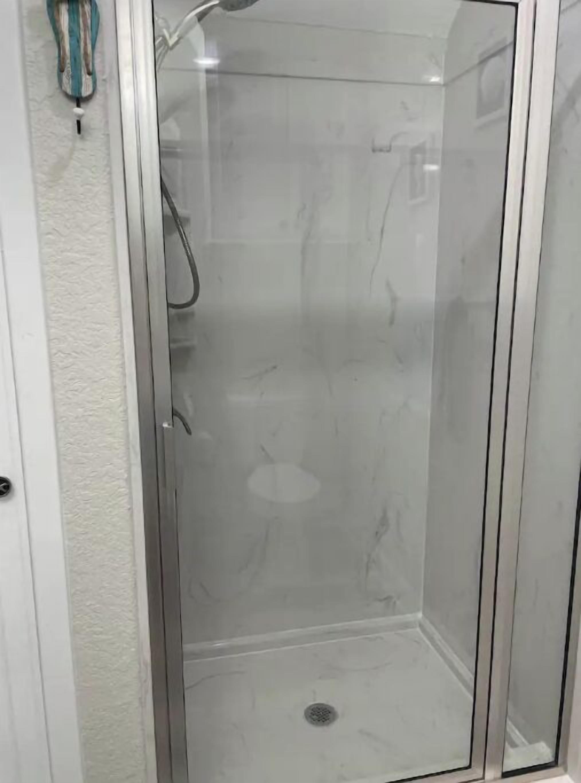 Une cabine de douche fermée par des parois de verre, avec un sol en marbre blanc et un petit drain au centre.