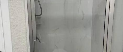 Une cabine de douche fermée par des parois de verre, avec un sol en marbre blanc et un petit drain au centre.