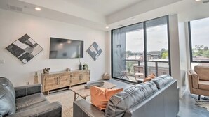 A modern living room with a large window, a flat-screen TV, and a leather sofa.