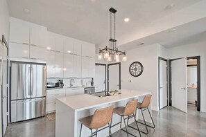 Una cocina moderna con armarios blancos, un refrigerador de acero inoxidable, una isla central con taburetes de bar e iluminación colgante.
