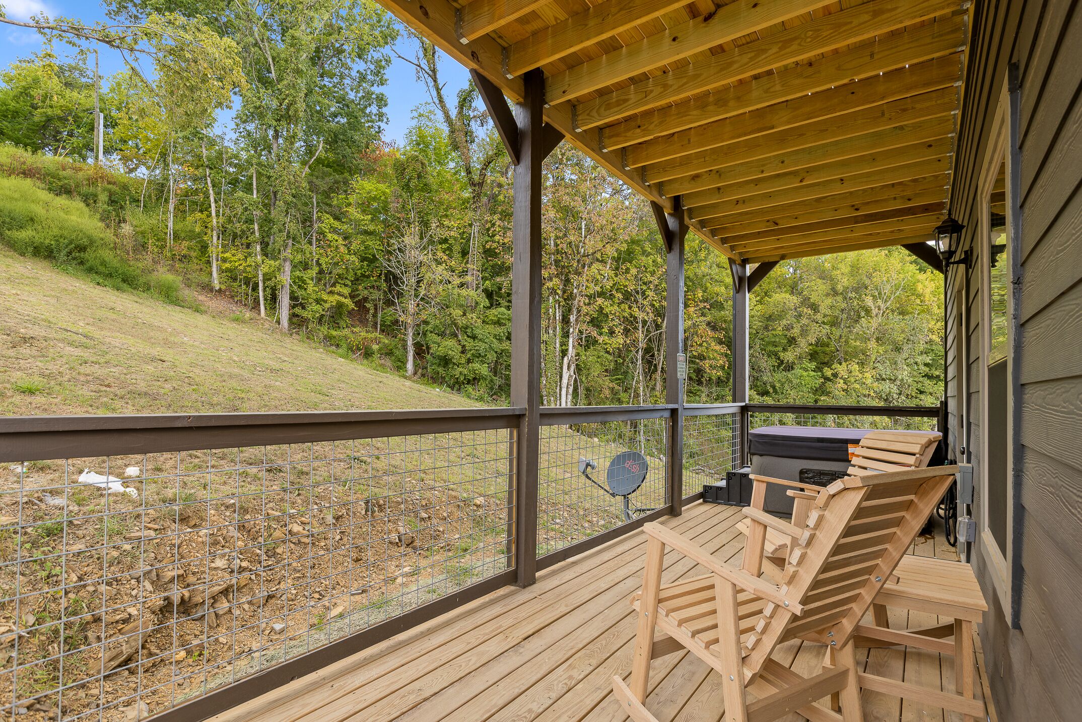 A covered outdoor deck with wooden chairs and a grill, overlooking a wooded area.