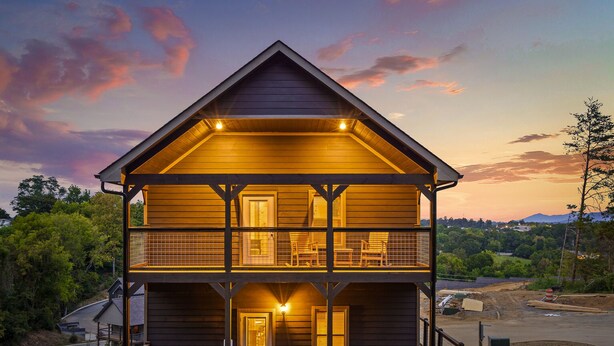 A two-story wooden cabin with a balcony on the upper floor, a porch with seating, and a scenic view of the surrounding landscape.