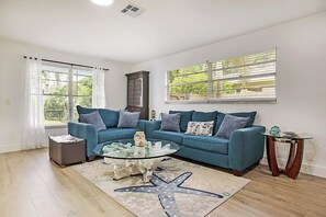 A living room with a blue sofa, glass coffee table, and a starfish rug.