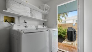 A laundry room with two white Samsung washing machines, a shelf with folded towels, a basket, and a starfish decoration.
