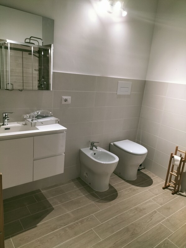 Un baño moderno con lavamanos, bidé, inodoro y un espejo sobre el lavamanos.