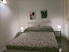 Una cama bien hecha con un edredón estampado, dos lámparas de noche y dos obras de arte en la pared.