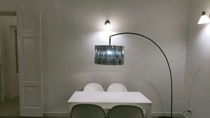 Ein Essbereich mit einem weißen Tisch und Stühlen, einer Stehlampe und einer Couch.