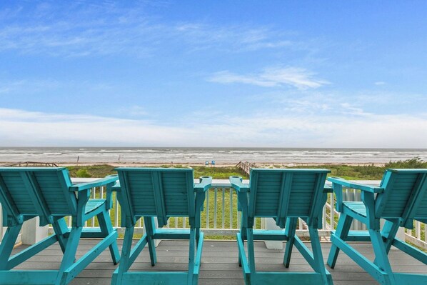 A view of the ocean from a wooden deck with four turquoise chairs facing the water.