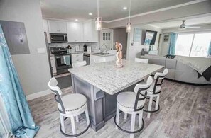 A modern kitchen with a central island, white cabinetry, and a dining area with four chairs.