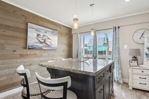 A kitchen with a wooden wall, a large island with a granite countertop, two chairs, pendant lights, a clock, and a Wi-Fi sign.