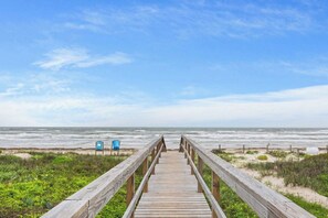 A wooden boardwalk leading to a beach with a clear sky.