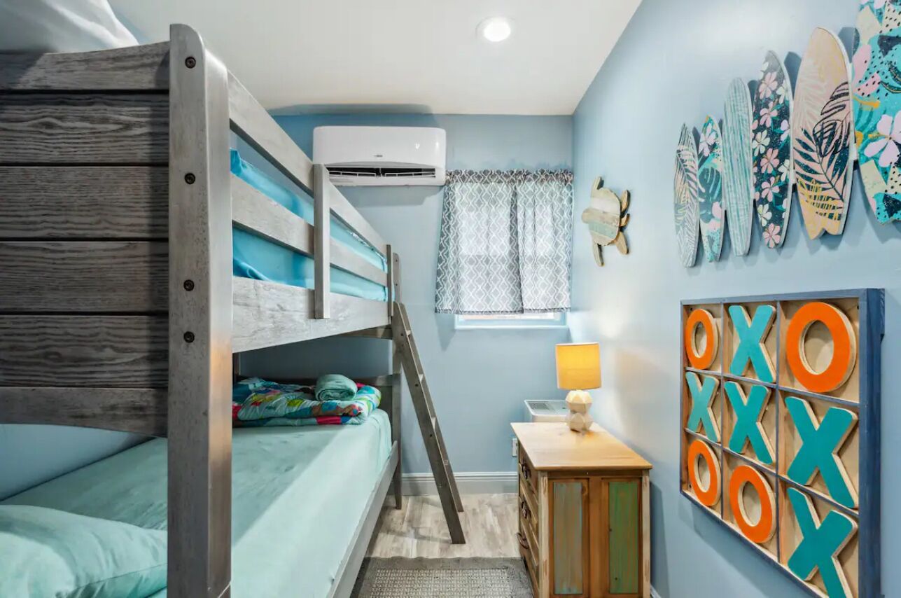 Camera con letto a castello, scaletta, condizionatore d'aria, finestra con tende a motivi e parete decorata con lettere dell'alfabeto.