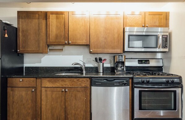 A kitchen with wooden cabinets, a stainless steel dishwasher, a stove, and a microwave.