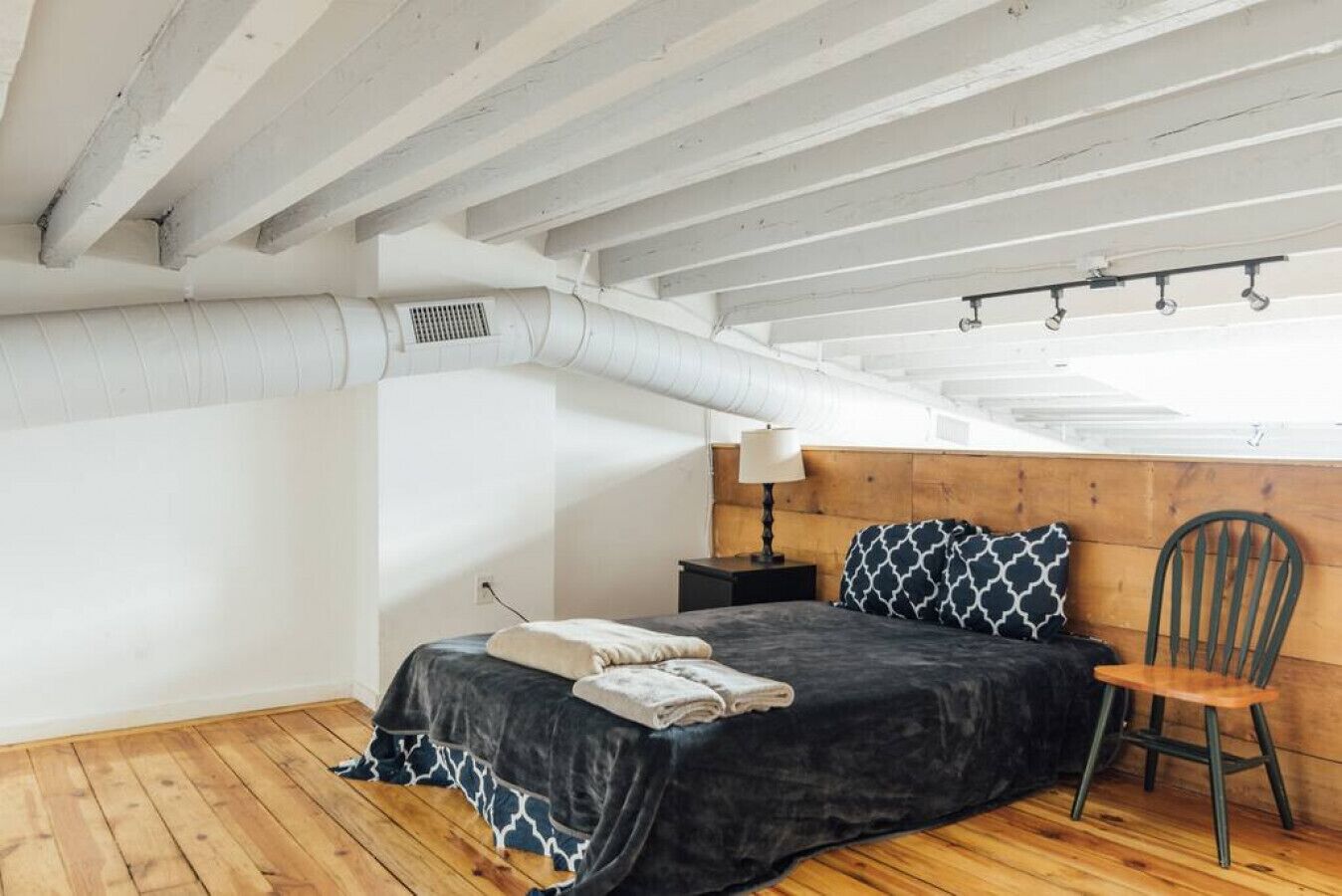 A bedroom with a bed, a chair, a nightstand, and a window.