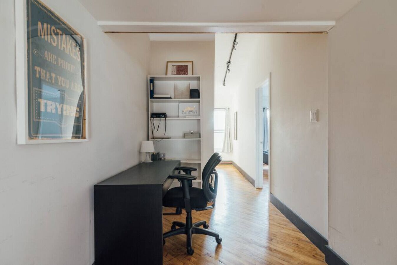 A narrow hallway with a desk and office chair, a bookshelf, and a framed quote on the wall.
