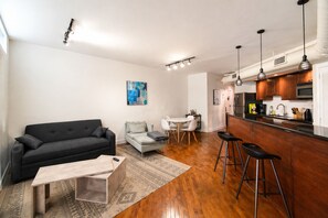 Ein modernes Wohnzimmer mit einer Couch, einem Couchtisch, einer Essecke mit Tisch und Stühlen sowie einer Küche mit Barbereich.