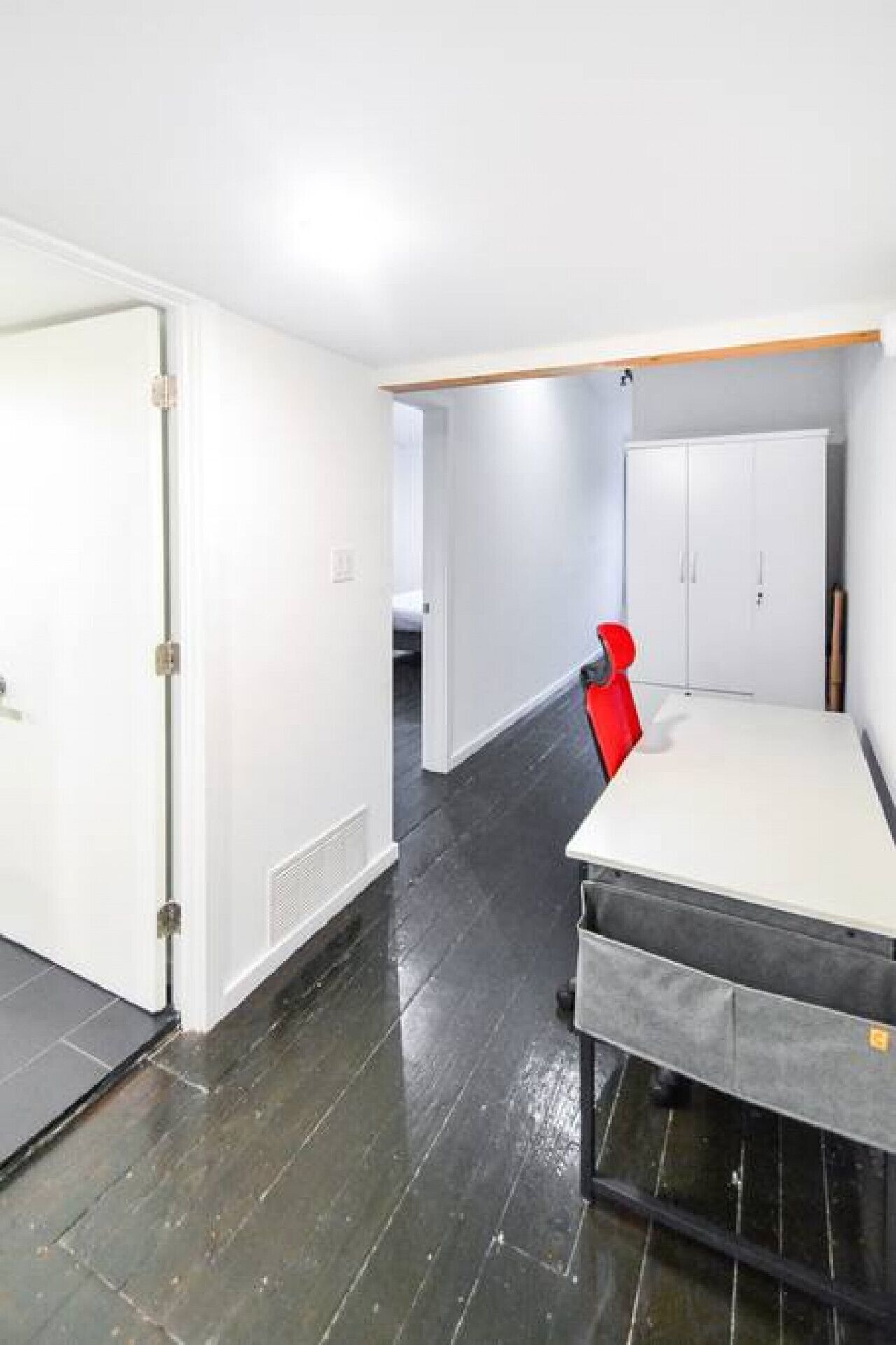 A room with a white wardrobe, a red chair, and a bed with a grey mattress.