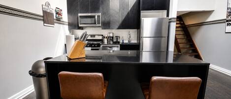 A modern kitchen with a black island, stainless steel appliances, and two leather bar stools.