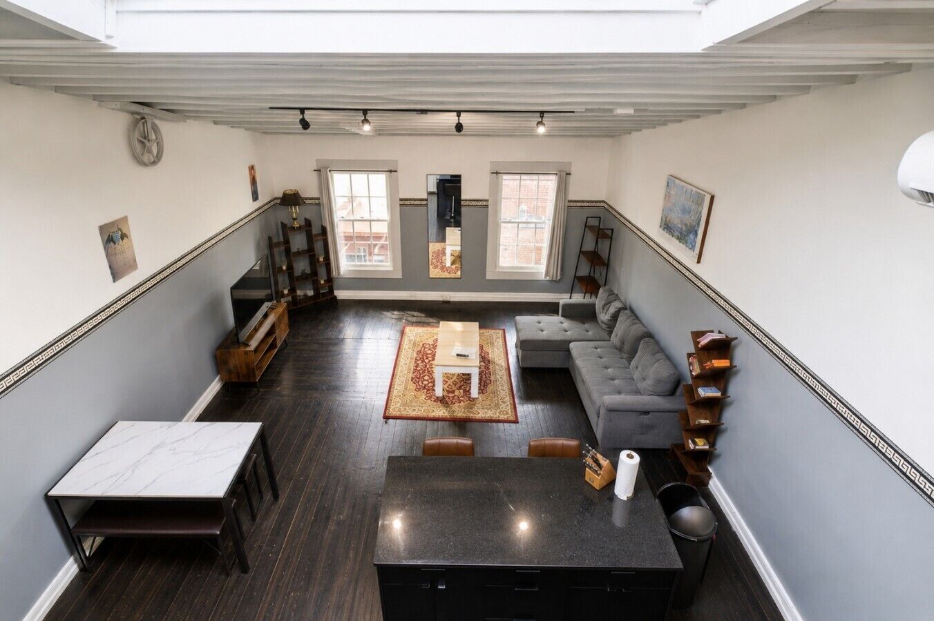 A spacious living area with a dark wood floor, a grey sectional sofa, a coffee table, and a TV.