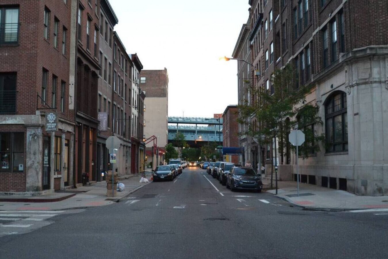 A street view with brick buildings, parked cars, and a pedestrian crossing.