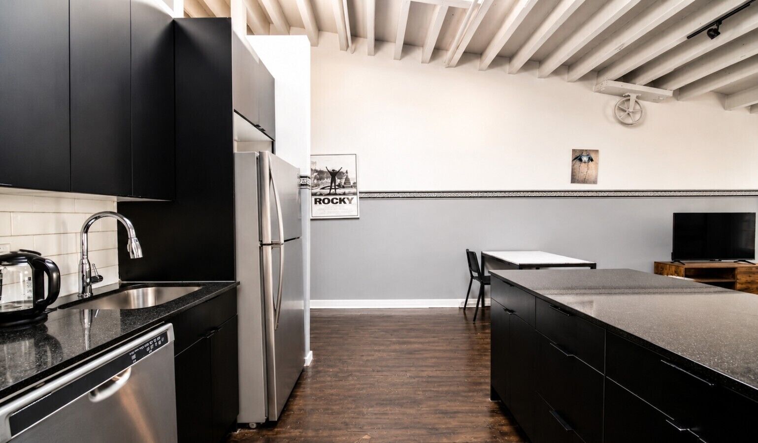 A modern kitchen with black cabinets, stainless steel appliances, and a wooden floor.
