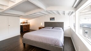 A bedroom with a bed, a dresser, a nightstand, and a window with a view.