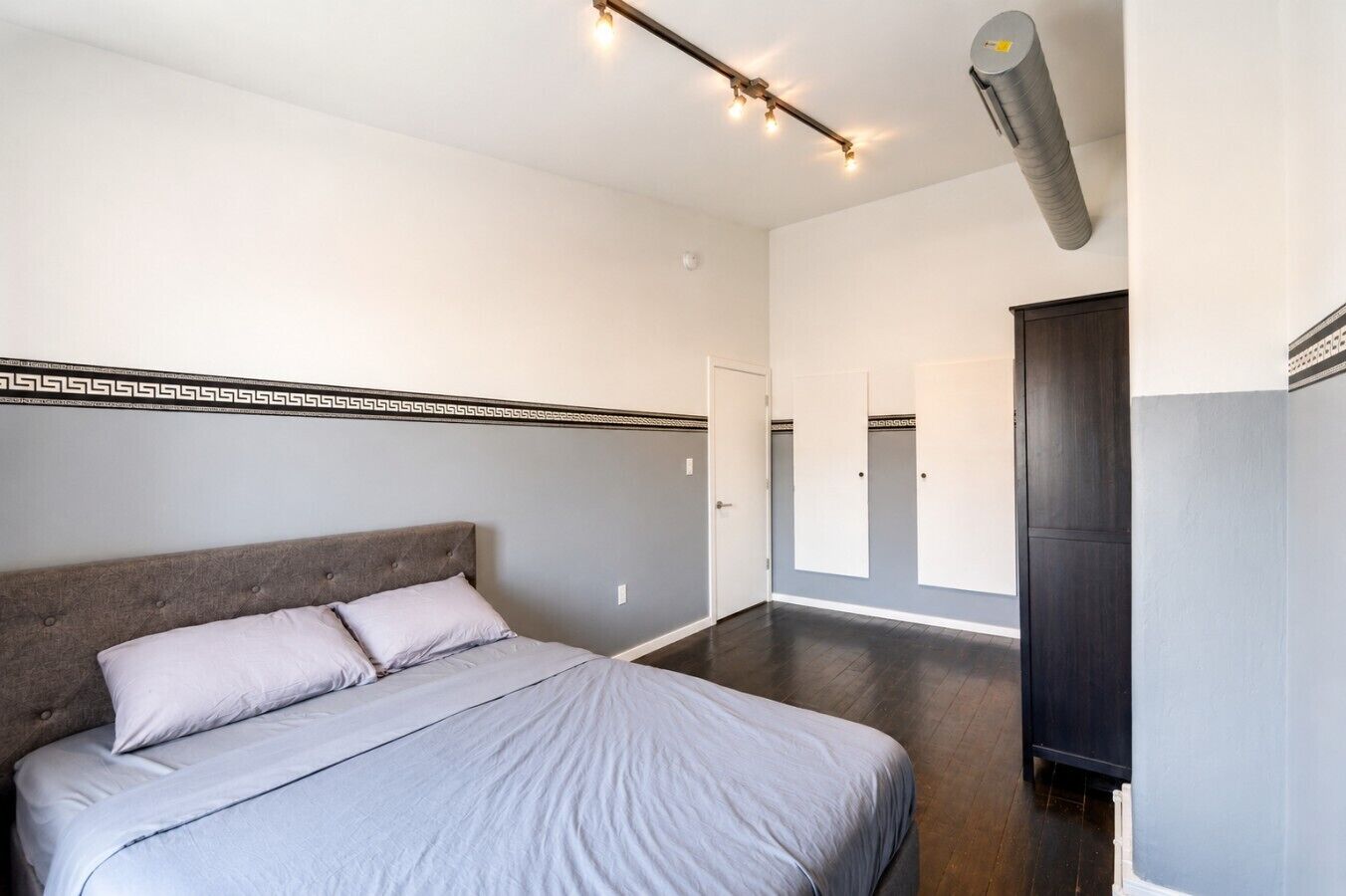 Un dormitorio con una cama, cabecera, aire acondicionado de pared y un pasillo que conduce a una puerta.