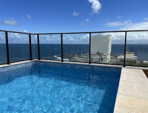 A pool with a clear view of the ocean and a tall building in the background.