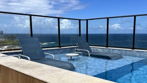 A rooftop infinity pool with two lounge chairs and a clear view of the ocean. - Sofisticado Loft Vista Mar - Farol da Barra (Salvador)