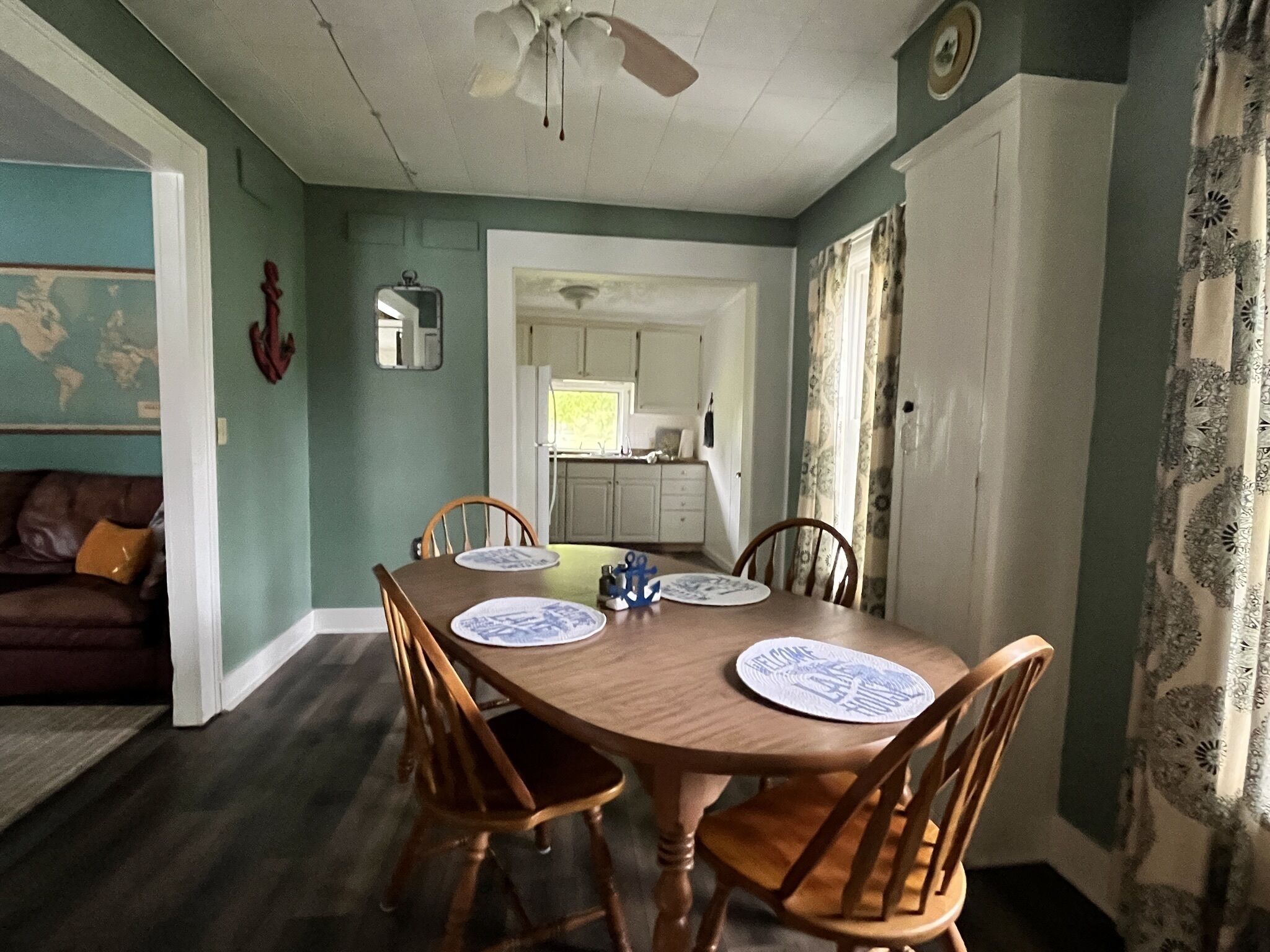 A dining area with a wooden table and four chairs, a ceiling fan, and a view into the kitchen.