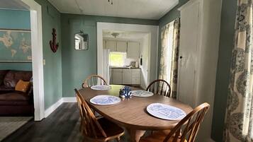 A dining area with a wooden table and four chairs, a ceiling fan, and a view into the kitchen.