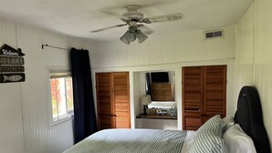 A bedroom with a bed, a nightstand, a dresser, a ceiling fan, and a window with curtains. - Cottages on Sand Lake - The Lazy Lakehouse (Nottawa)
