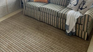 A living room with a striped sofa, a small side table, and a view of a dock and water through large windows. - Cottages on Sand Lake - The Lazy Lakehouse (Nottawa)