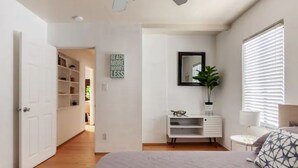 Une chambre à coucher comprenant un lit, une table de chevet, un miroir, une étagère et une porte donnant sur une autre pièce.
