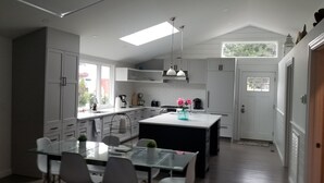 Une cuisine moderne avec des armoires blanches, un îlot central, des luminaires suspendus et une vue sur l’extérieur.