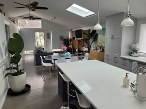 Una cocina moderna con una isla central, muebles blancos y un comedor con mesa y sillas de vidrio.