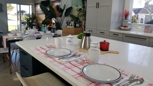 Une cuisine moderne dotée d’un îlot central, de meubles blancs et d’un coin repas avec une table dressée pour deux personnes.