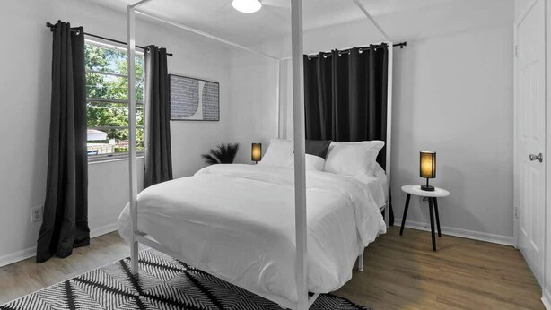 A modern bedroom with a four-poster bed, a ceiling fan, two bedside lamps, and a view of the outdoors.