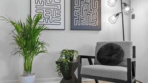 A modern interior with a grey upholstered chair, a black floor lamp, and two wall-mounted abstract art pieces.