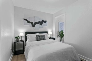 Una camera da letto ordinata con un letto, due comodini con lampade, un'opera d'arte appesa al muro e una porta.