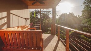 Um banco de madeira numa varanda com guarda-corpo, escadas e vista para o verde.